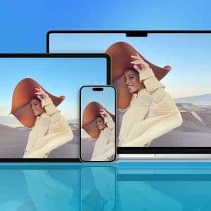 A tablet, smartphone, and laptop display the same image of a smiling person in a large hat and beige outfit, set against a blue gradient background with the Apple logo in the corner—highlighting seamless iCloud syncing across devices.