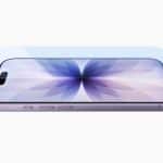 A smartphone with a purple flower design on its screen, featuring durable Apple Corning glass, lies flat with a transparent screen protector aligned above it. The phone is viewed from an angled side perspective on a white background.