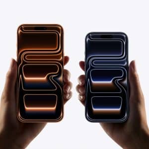 Two hands hold smartphones side by side. The left phone displays orange glowing lines on a black screen, while the right shows blue glowing lines. Both feature sleek designs and smooth visuals, thanks to advanced ProMotion scaling technology.
