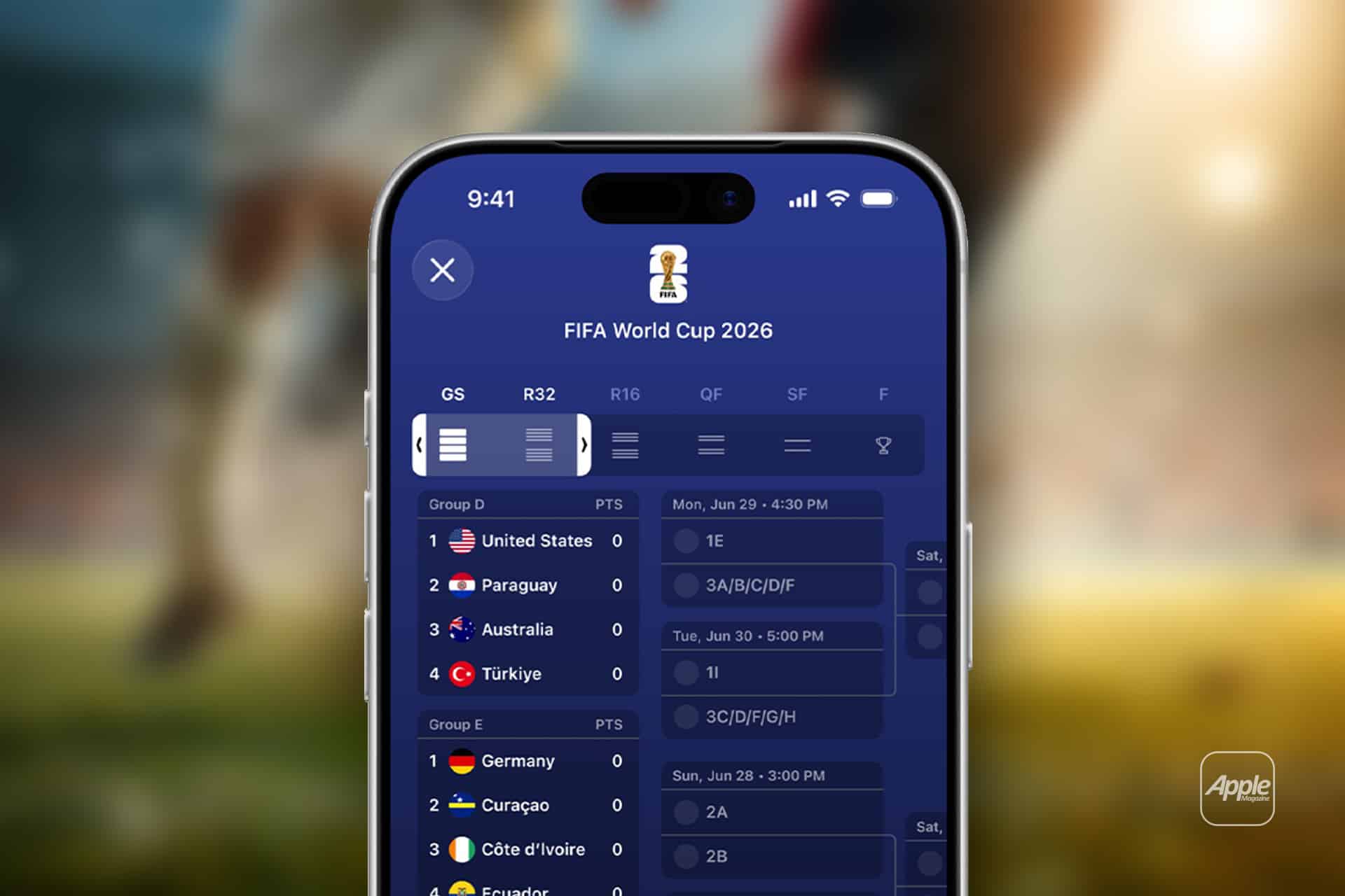 Close-up of a smartphone using Live Activities in the Apple Sports app to display the FIFA World Cup 2026 schedule, highlighting group stage matches for the United States, Paraguay, Australia, and Turkey. A blurred soccer field and players fill the background.