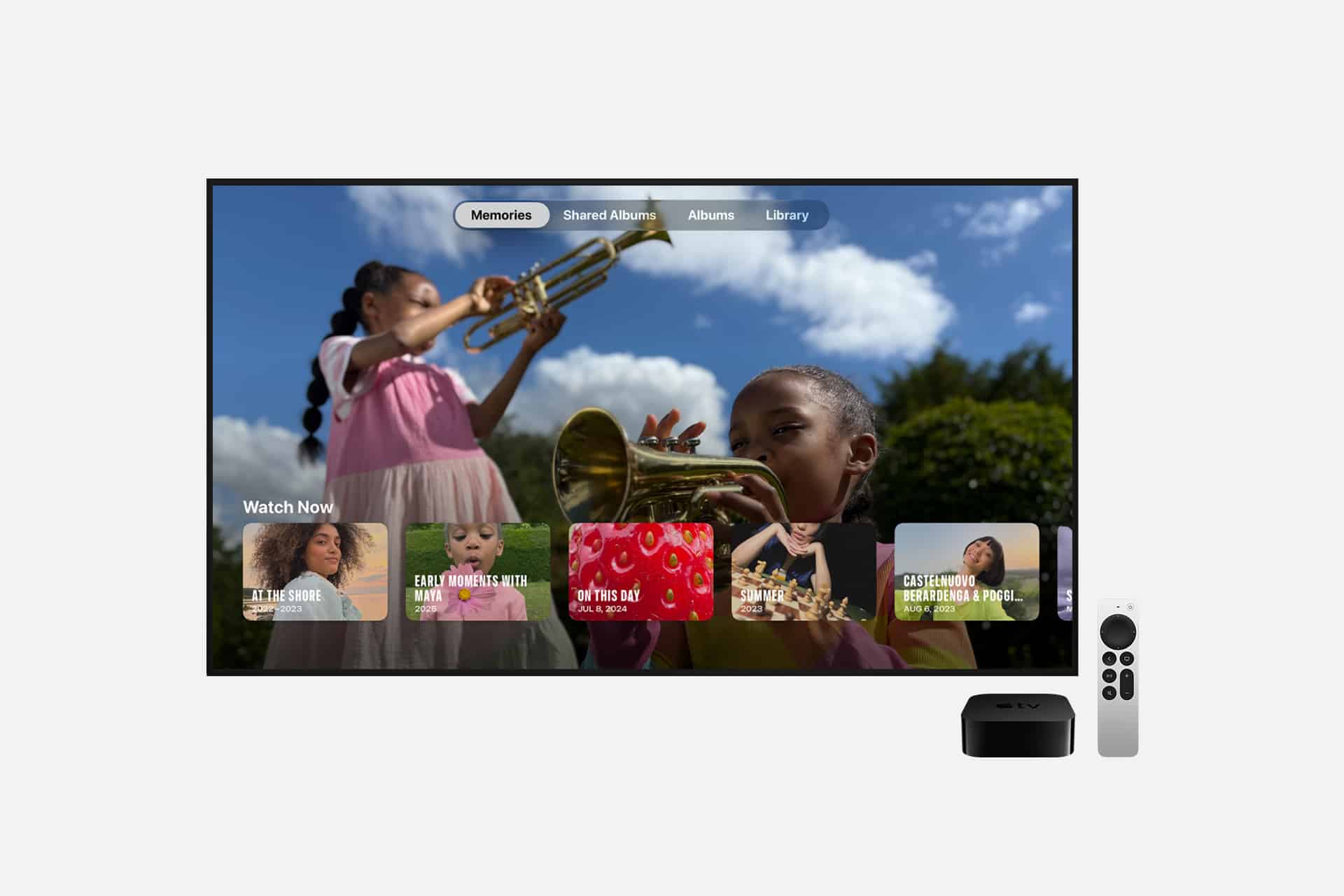 A TV displays a photo memories interface with children playing trumpets, with an Apple TV device and remote shown beside it.