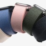 Five smartwatches with woven nylon bands—perfect Apple accessories—in beige, blue, pink, green, and black are arranged in a row against a white background.
