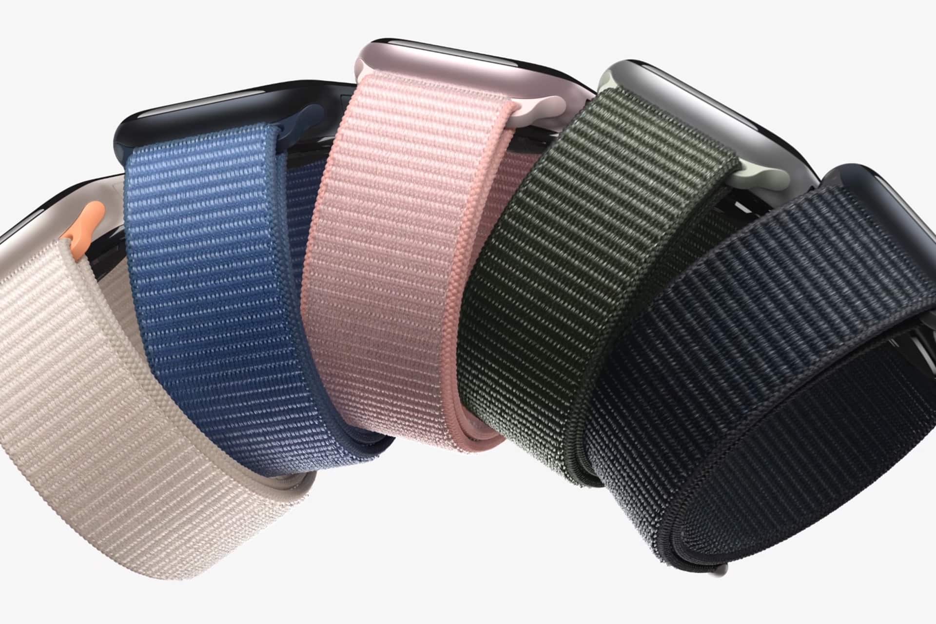 Five smartwatches with woven nylon bands—perfect Apple accessories—in beige, blue, pink, green, and black are arranged in a row against a white background.