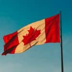 A Canadian flag with a red maple leaf in the center flutters on a flagpole against a clear blue sky, symbolizing security much like Apple encryption.
