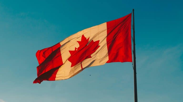 A Canadian flag with a red maple leaf in the center flutters on a flagpole against a clear blue sky, symbolizing security much like Apple encryption.