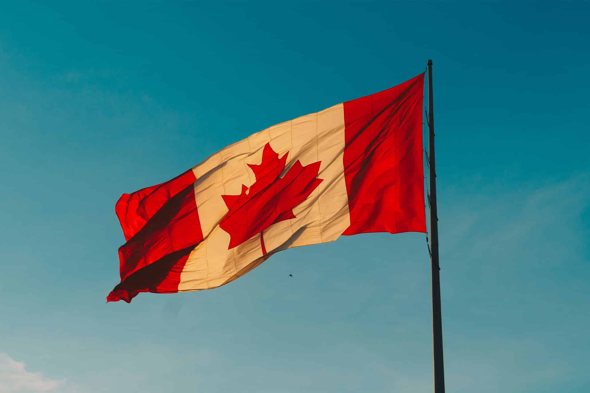 A Canadian flag with a red maple leaf in the center flutters on a flagpole against a clear blue sky, symbolizing security much like Apple encryption.
