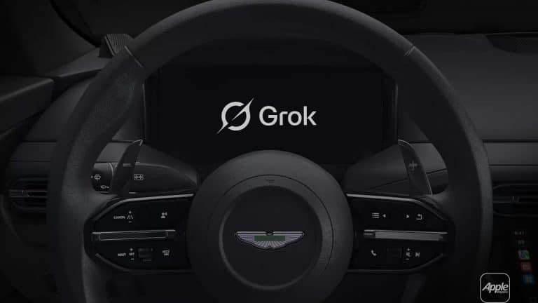 A car steering wheel with the Aston Martin logo, dashboard controls, and a central display screen showing "Grok Voice" with its logo. An Apple logo appears in the lower right corner.