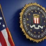 A large FBI seal is mounted on a blue wall next to a partially visible American flag, echoing the values of "Fidelity, Bravery, Integrity"—much like the rigorous standards set by each iOS security update, including iOS 15.8.8 and iOS 16.7.16.