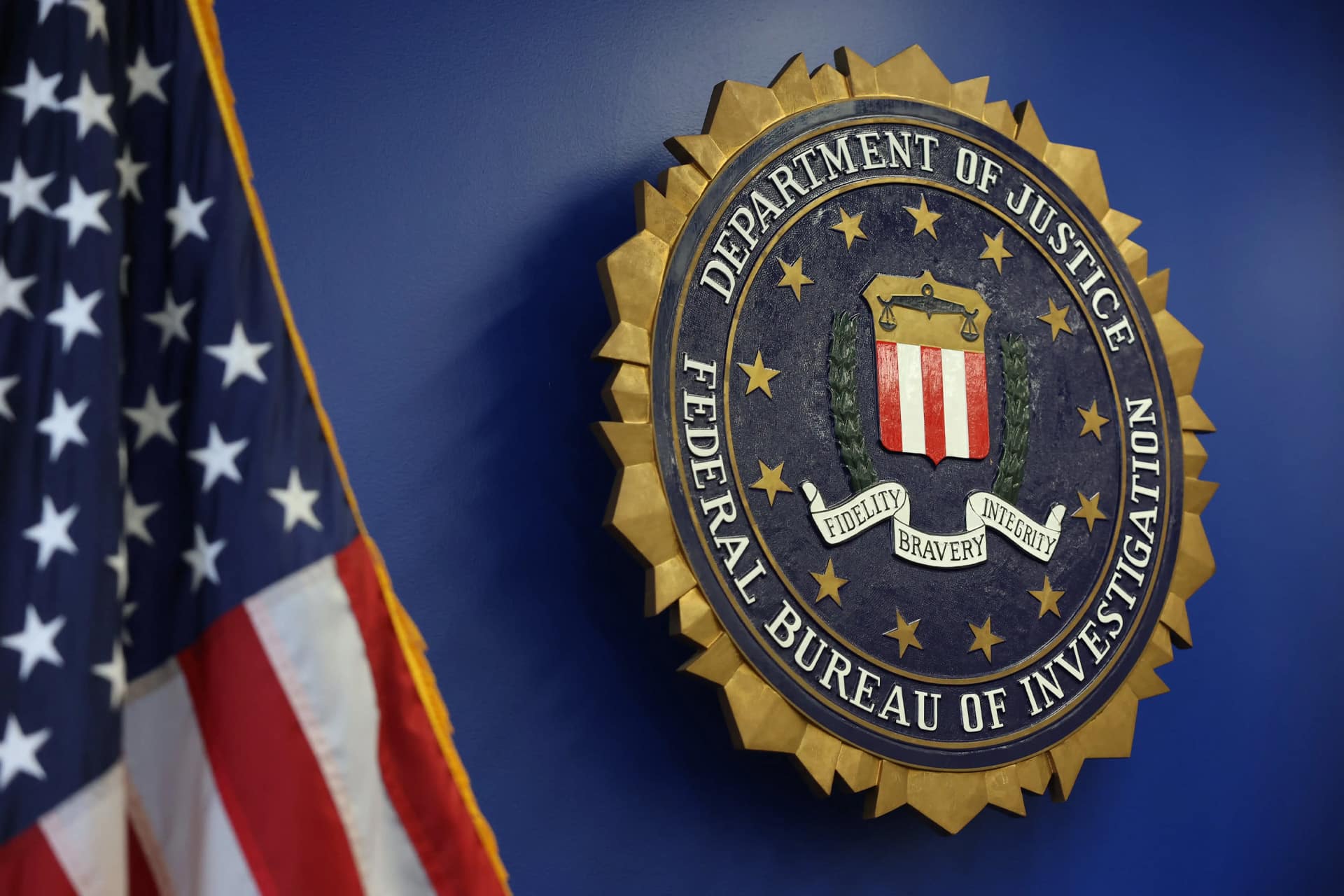 A large FBI seal is mounted on a blue wall next to a partially visible American flag, echoing the values of "Fidelity, Bravery, Integrity"—much like the rigorous standards set by each iOS security update, including iOS 15.8.8 and iOS 16.7.16.