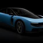 A sleek, blue sports car with a matte finish, black accents, and tinted windows, shown on a black background. Aerodynamic curves hint at Jony Ive-inspired design, while a prominent grille and yellow badge evoke the innovative Ferrari Luce spirit.