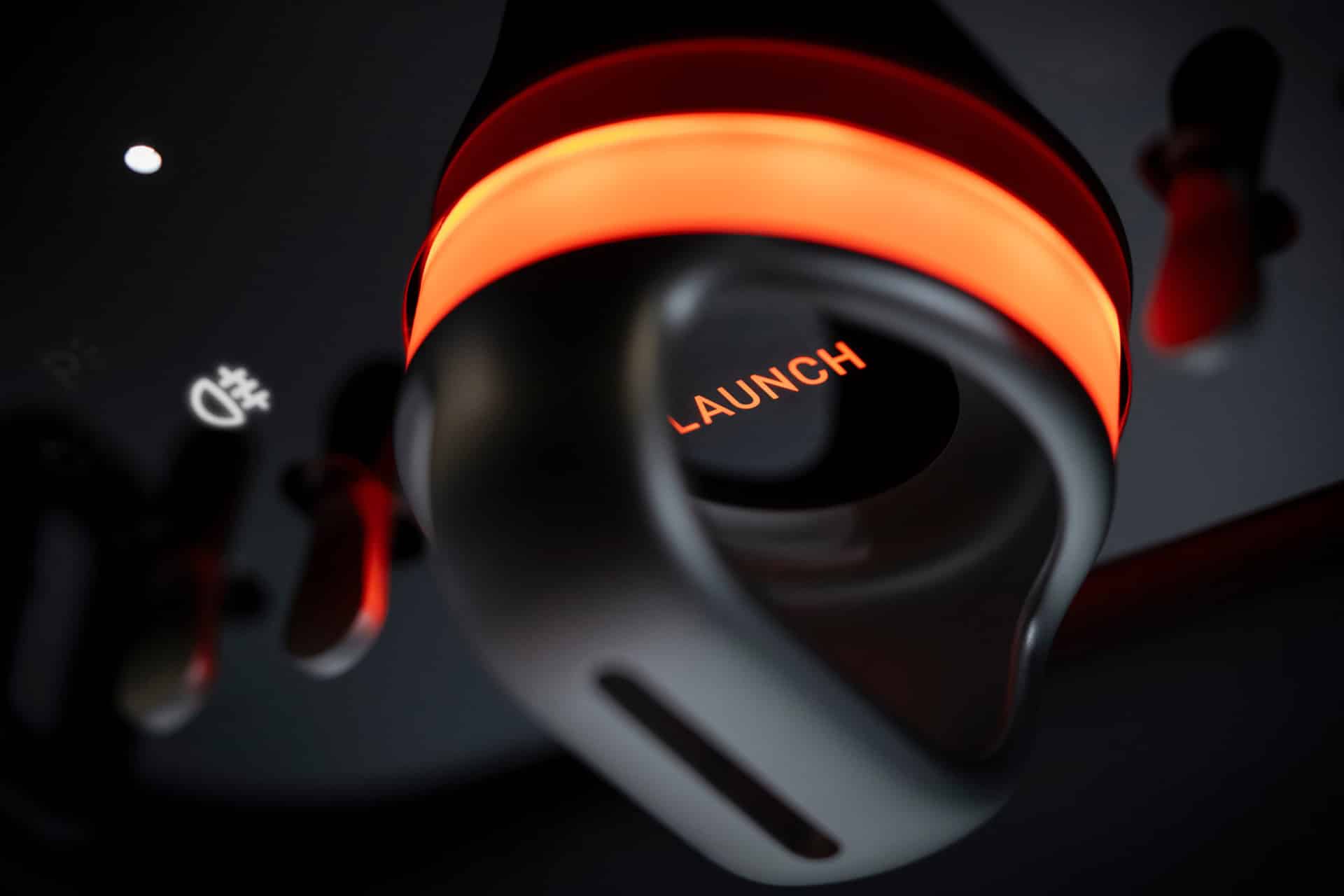 Close-up of a black and orange "LAUNCH" lever with illuminated ring, surrounded by control switches, evoking a high-tech panel reminiscent of Jony Ive’s design for Ferrari Luce CarPlay or the advanced CarPlay Ultra interface.