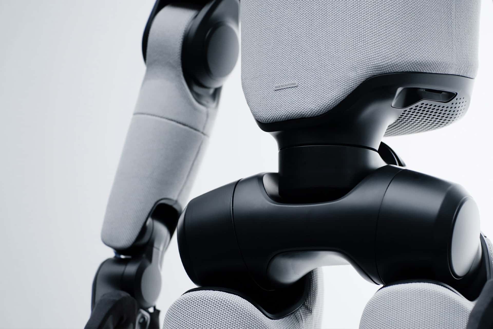 Close-up of Figure AI’s F.03 robot arm and torso, featuring smooth black joints and light gray fabric-covered surfaces in a sleek, minimalistic design—an innovation recently highlighted after the Apple acquisition, set against a light background.