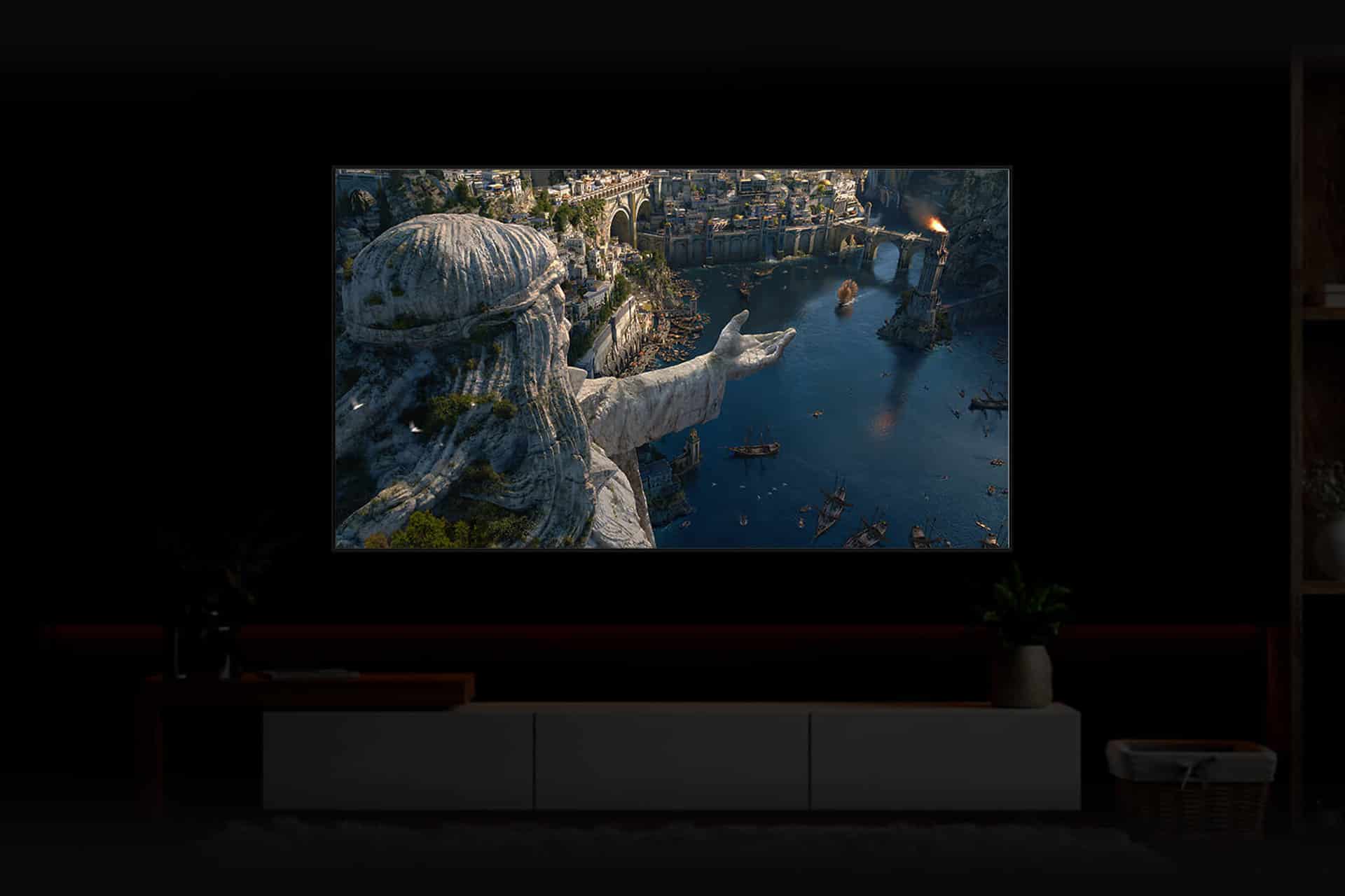 A large screen powered by Eclipsa Video and HDR10+ Technologies displays a fantasy city where a colossal stone statue overlooks a river lined with boats and cliffside buildings. The dark room features minimal furniture and decor below the screen.