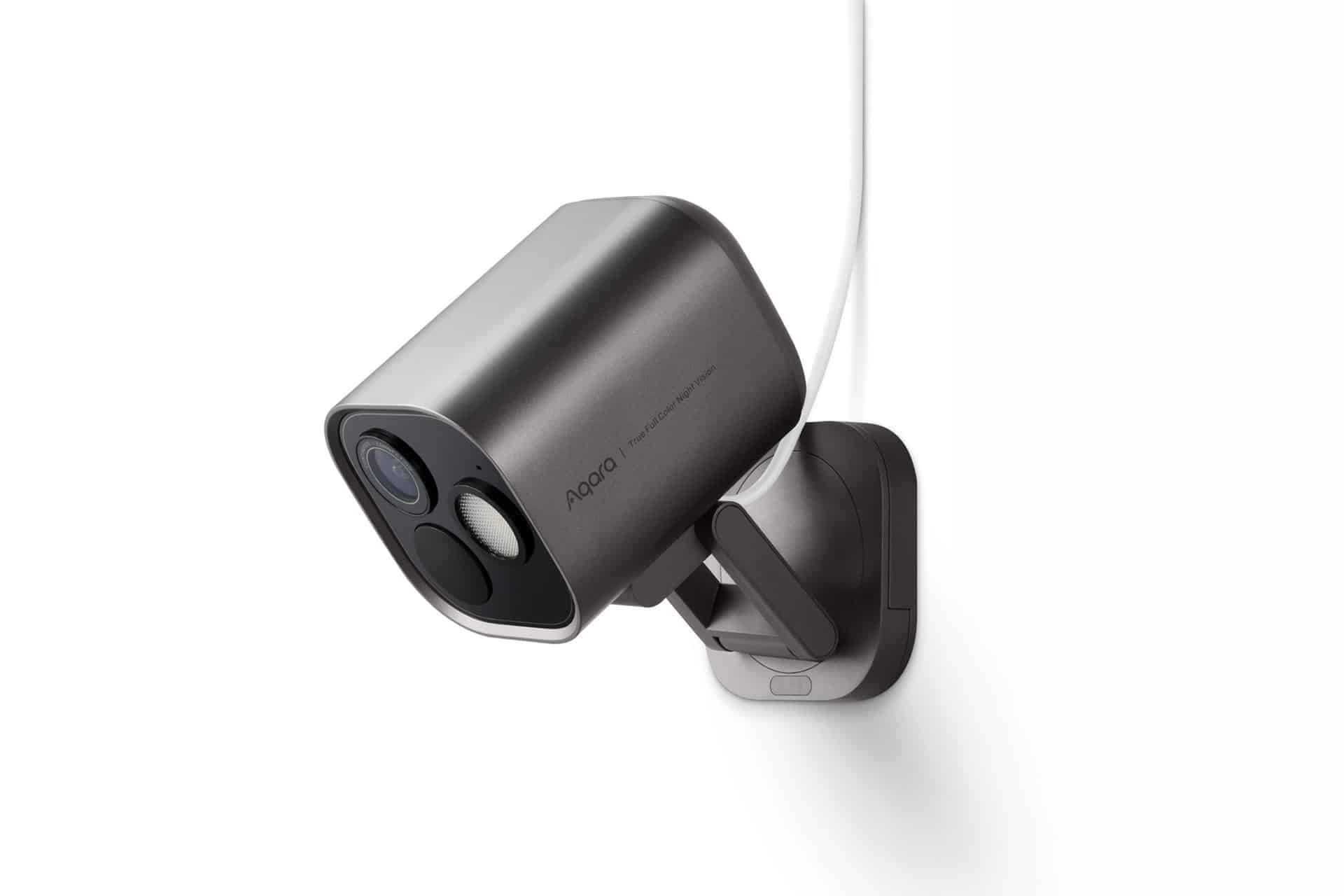 A sleek, modern security camera with a metallic finish is mounted on a white wall, attached by a bracket and connected with a white cable—perfect for monitoring specific Home Activity Zones.
