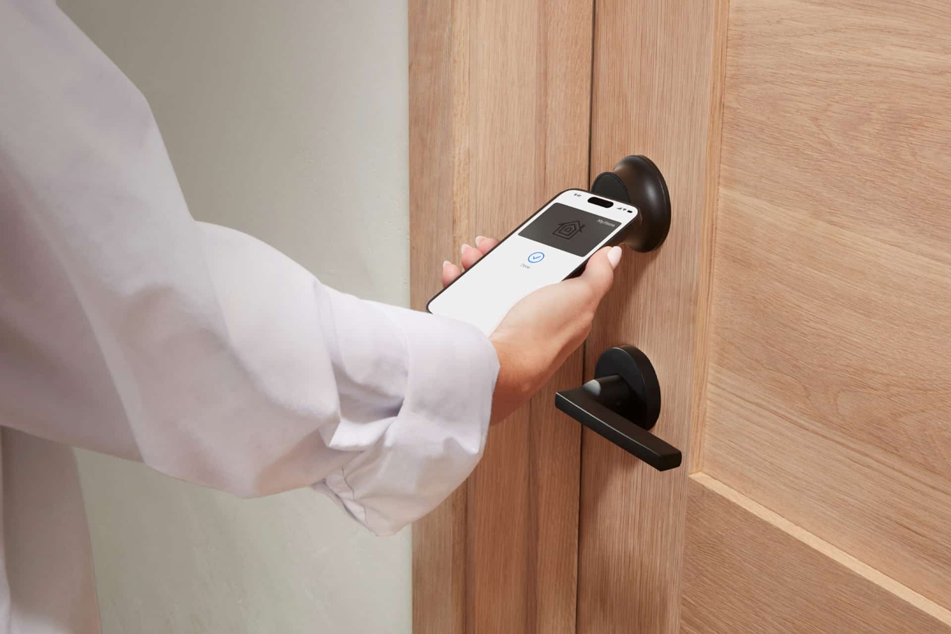 A person is holding a smartphone near a HomeKit smart lock, appearing to unlock the wooden door using a digital key or mobile access app.
