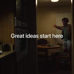 A person stands and gestures in a dimly lit kitchen-dining area, with the words "Great ideas start here" overlaid in white text—perfect inspiration for Mac Students seeking creativity at home.