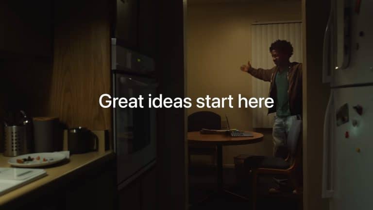 A person stands and gestures in a dimly lit kitchen-dining area, with the words "Great ideas start here" overlaid in white text—perfect inspiration for Mac Students seeking creativity at home.
