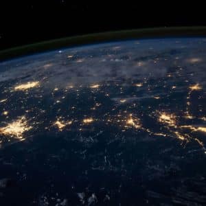 A view of Earth from space at night, illuminated by city lights and framed by clouds, captures the planet’s curvature beneath the dark sky—an awe-inspiring perspective enhanced by Orbital AI technology.
