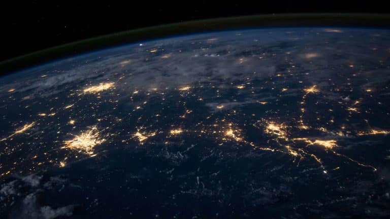 A view of Earth from space at night, illuminated by city lights and framed by clouds, captures the planet’s curvature beneath the dark sky—an awe-inspiring perspective enhanced by Orbital AI technology.