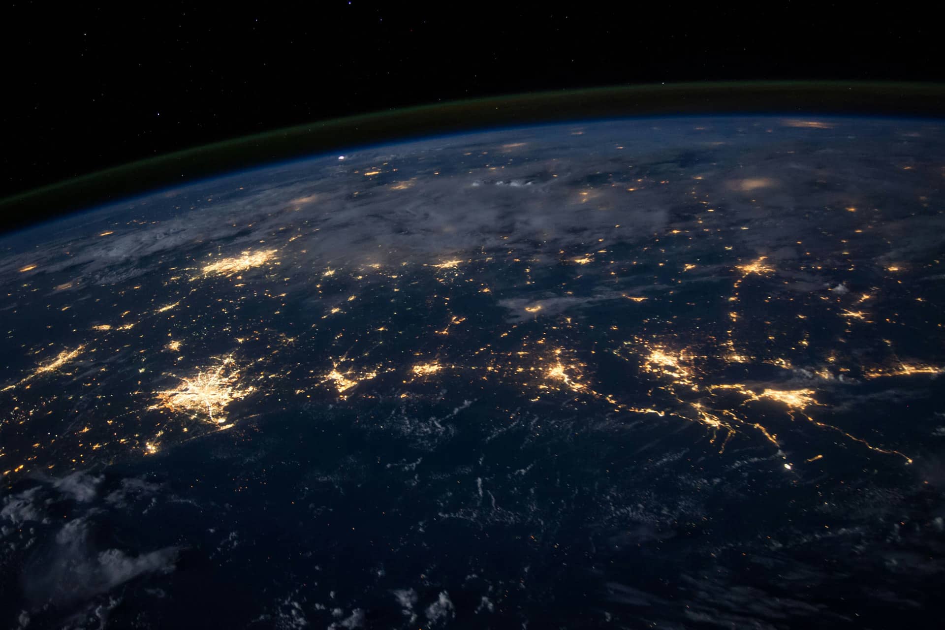 A view of Earth from space at night, illuminated by city lights and framed by clouds, captures the planet’s curvature beneath the dark sky—an awe-inspiring perspective enhanced by Orbital AI technology.
