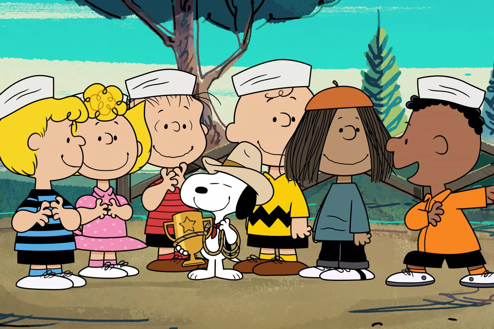 A group of Peanuts characters, including Snoopy holding a trophy, stand together outdoors smiling in sailor hats. Trees and a blue sky are visible in the background, capturing the charm of Peanuts on Apple TV.