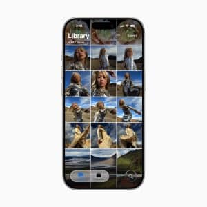 A smartphone screen showcases the iOS 26 Photos layout in a gallery app, featuring several images of a woman outdoors in a shiny silver outfit, set against mountains and fields.