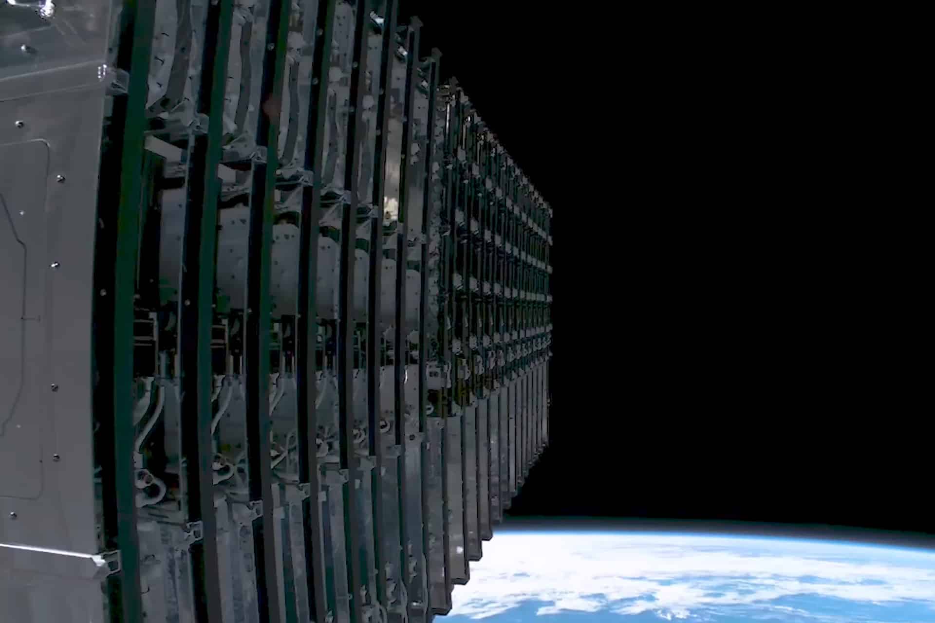 A close-up view of a stack of SpaceX Starlink satellites in orbit above Earth, with the blue and white curve of the planet visible against the blackness of space—hinting at future iPhone satellite connectivity.