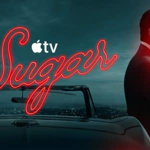 A man in a suit and sunglasses leans on a convertible car at dusk. The word "Sugar" glows in neon, with the Apple TV+ logo and hints of Sugar season 2 as the city skyline shines behind him.