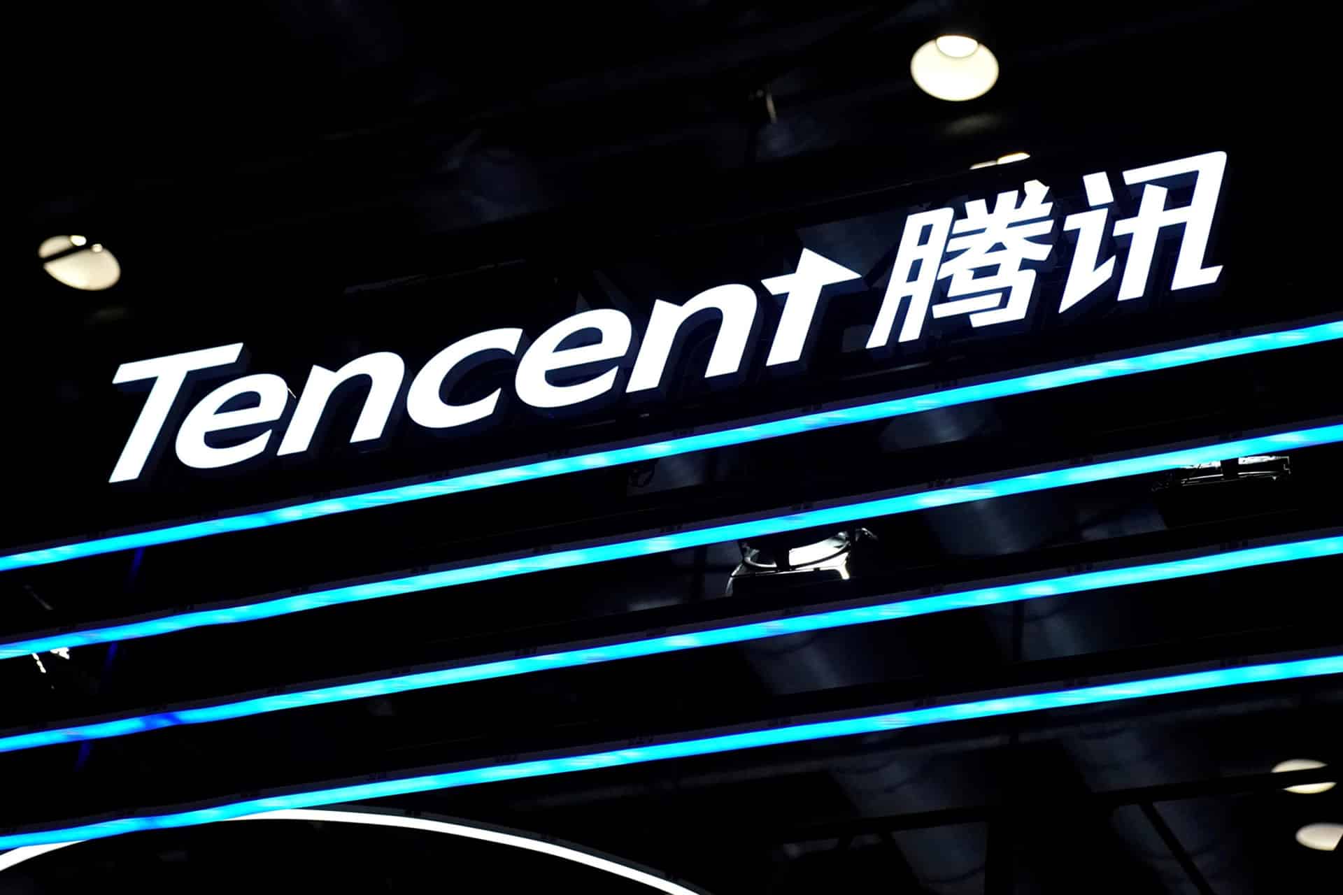 A Tencent sign with the company name in English and Chinese, illuminated in white and blue, is displayed against a dark background with ceiling lights above, evoking the modern tech presence of giants like Tencent and NetEase.