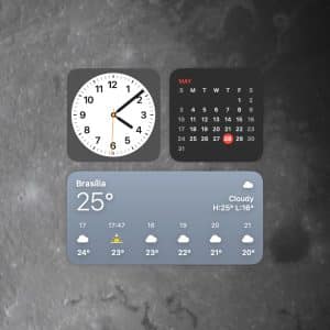 A digital interface with Mac desktop widgets displays a clock at 9:07, a May calendar highlighting the 28th, and a weather widget for Brasília showing 25°C and cloudy skies, all set against the moon’s surface.
