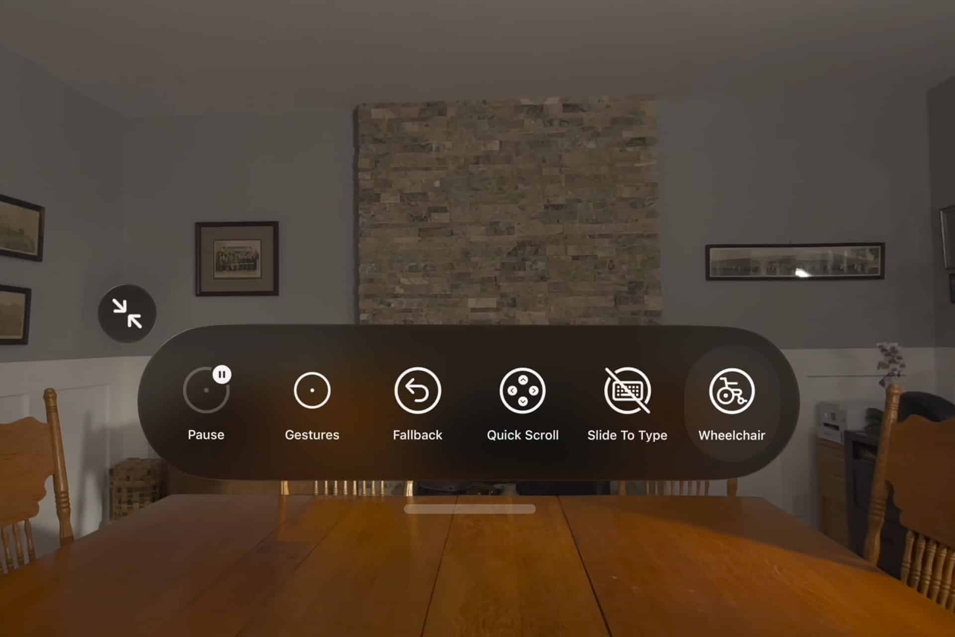 A virtual menu with accessibility options, including Pause, Gestures, Fallback, Quick Scroll, Slide To Type, and Vision Pro wheelchair, is displayed over a dining room table with wooden chairs and a stone fireplace.