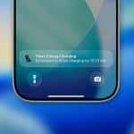 Close-up of an iPhone screen showing a notification for “Clean Energy Charging,” scheduled to finish by 10:13 AM. Flashlight and camera icons are visible on the lock screen, set against a blue and green background, highlighting iPhone clean energy features.