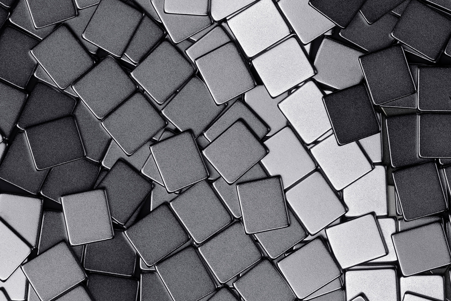 A close-up view of numerous small, square metallic tiles arranged in a scattered, overlapping pattern, resembling the sleek design often seen in Apple accessories, featuring various shades of gray and silver.