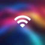 A white Mac Wi-Fi symbol is centered on a colorful, blurred gradient background with shades of pink, purple, blue, and yellow. The word "Apple" is in the bottom right corner.