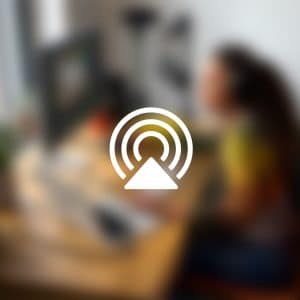 A blurred image of a person working at a computer desk with the Mac AirPlay icon overlaid in the center. The Apple logo appears in the bottom right corner, showcasing AirPlay display mirroring to an Apple TV.