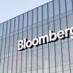 The exterior of a modern glass building with the word “Bloomberg” displayed in large white letters on the facade, where Mark Gurman often reports on trends like rising memory costs.