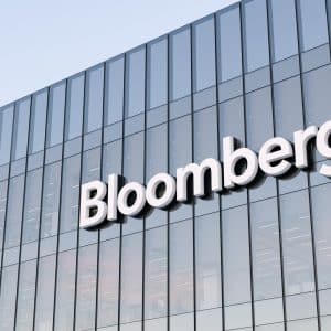 The exterior of a modern glass building with the word “Bloomberg” displayed in large white letters on the facade, where Mark Gurman often reports on trends like rising memory costs.