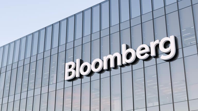 The exterior of a modern glass building with the word “Bloomberg” displayed in large white letters on the facade, where Mark Gurman often reports on trends like rising memory costs.