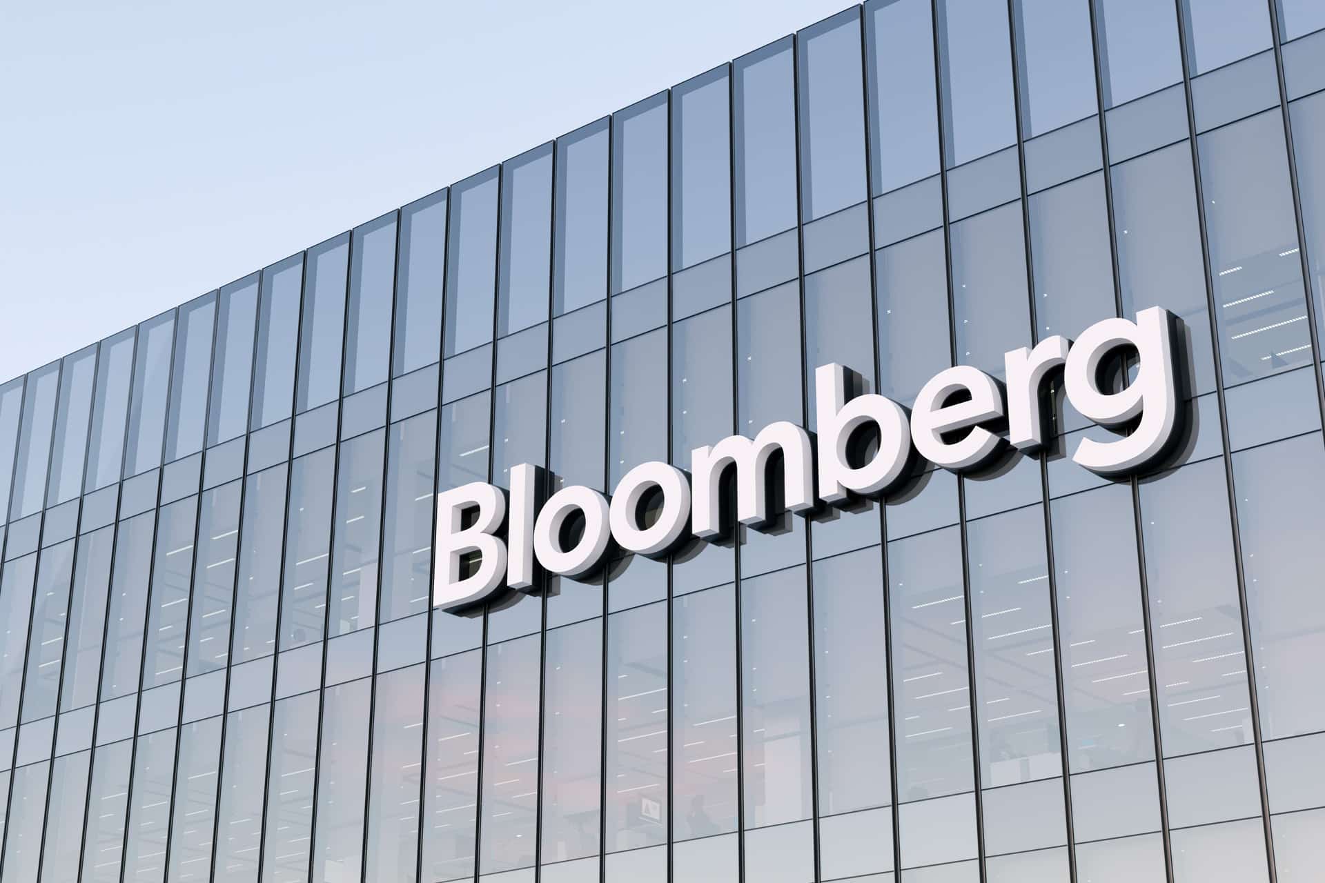 The exterior of a modern glass building with the word “Bloomberg” displayed in large white letters on the facade, where Mark Gurman often reports on trends like rising memory costs.