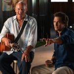 Brothers - Two brothers sit indoors; one, resembling Matthew McConaughey in a light floral shirt, smiles with a guitar, while the other gestures with his drink. A classic car peeks from the background—an Apple Originals vibe.