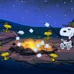 Snoopy and several yellow birds wearing scout hats roast marshmallows over a campfire at night in a forest, capturing a classic Peanuts moment sure to delight Charlie Brown fans and Apple TV viewers alike.
