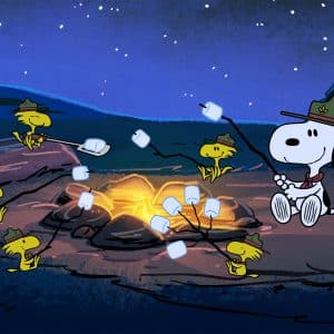Snoopy and several yellow birds wearing scout hats roast marshmallows over a campfire at night in a forest, capturing a classic Peanuts moment sure to delight Charlie Brown fans and Apple TV viewers alike.