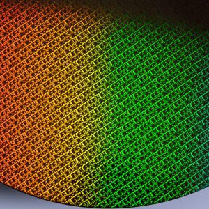 A close-up of a silicon wafer with a grid pattern reflecting a gradient of colors from orange to green to blue, highlighting the intricate design found in Apple chips and advanced M-series chips.