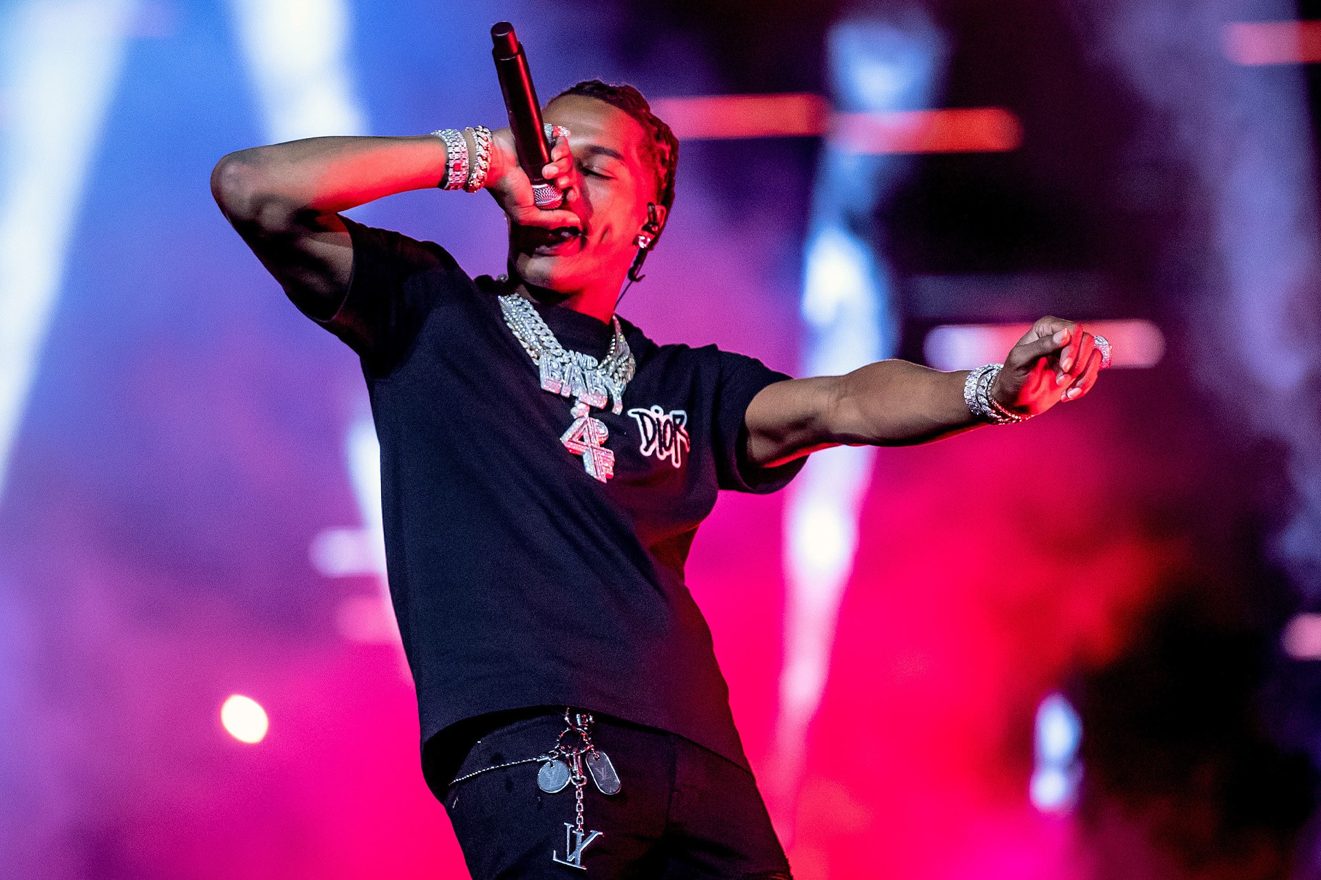 A performer wearing a black shirt, multiple silver chains, and bracelets sings into a microphone on stage—surrounded by colorful pink and purple lights and smoke effects—capturing the vibrant energy of an Apple Music Future showcase.
