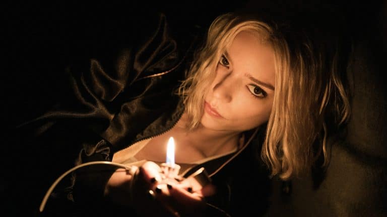 A woman with blonde hair and a serious expression lies in dim light, holding a lit lighter that illuminates her face and part of her black clothing, reminiscent of Anya Taylor-Joy in an Apple Studios' Lucky trailer.