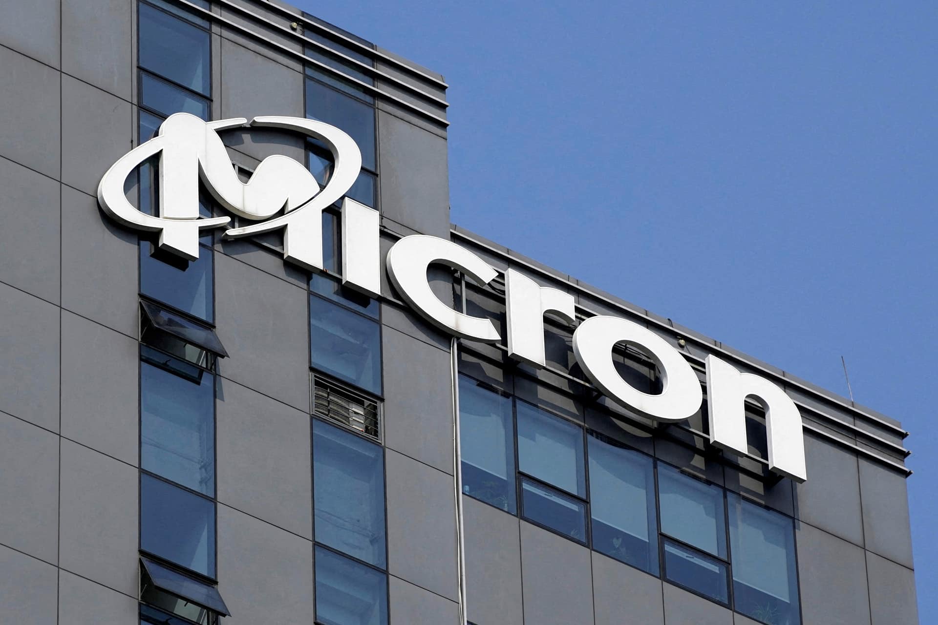 The exterior of a modern building with large windows, featuring the Micron logo and name prominently displayed near the top, highlights their leadership in NAND technology against a clear blue sky.