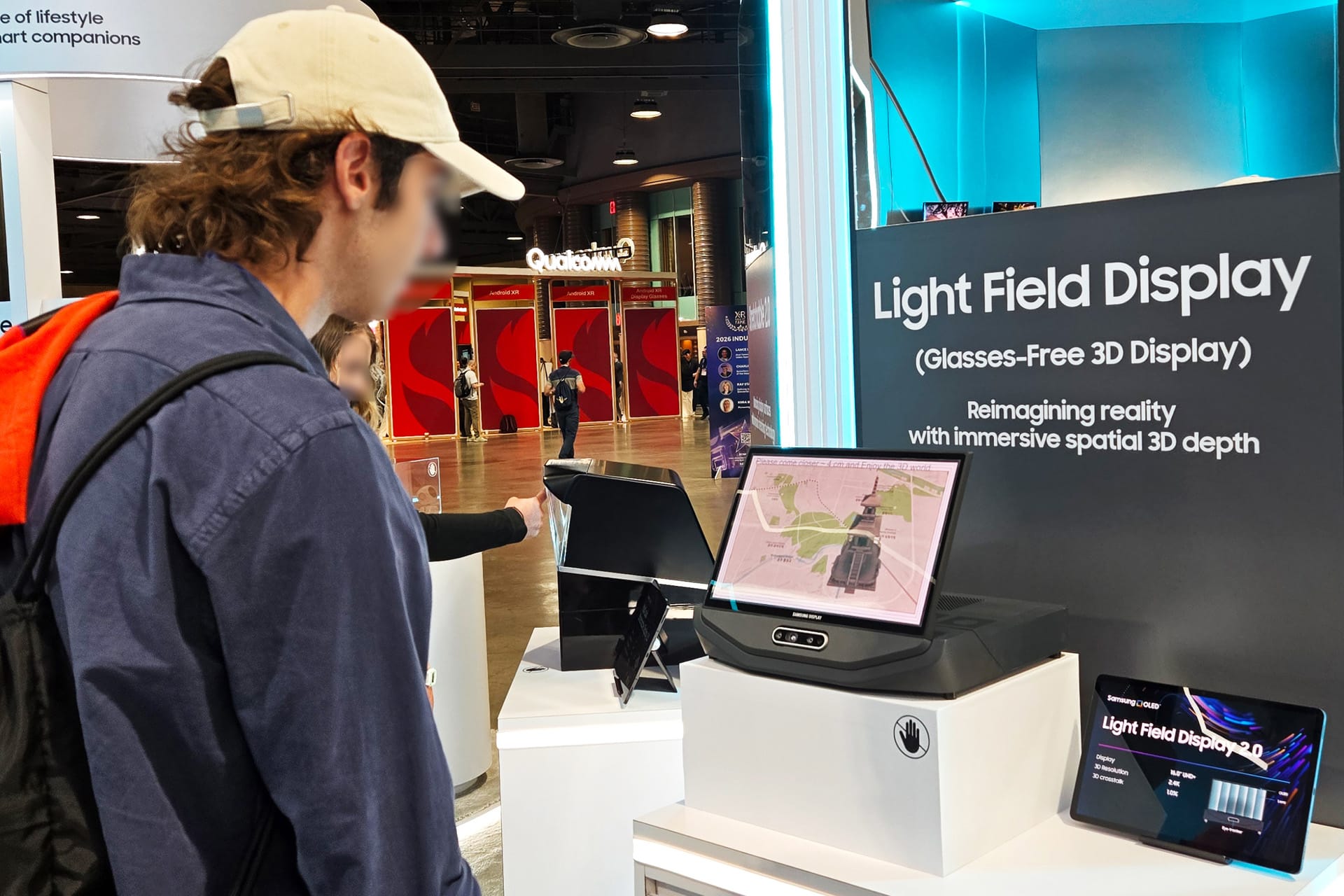 A person in a cap examines the “Light Field Display” exhibit, where a screen—featuring RGB OLEDoS technology—shows a 3D map. A sign highlights this glasses-free 3D experience with immersive spatial depth.