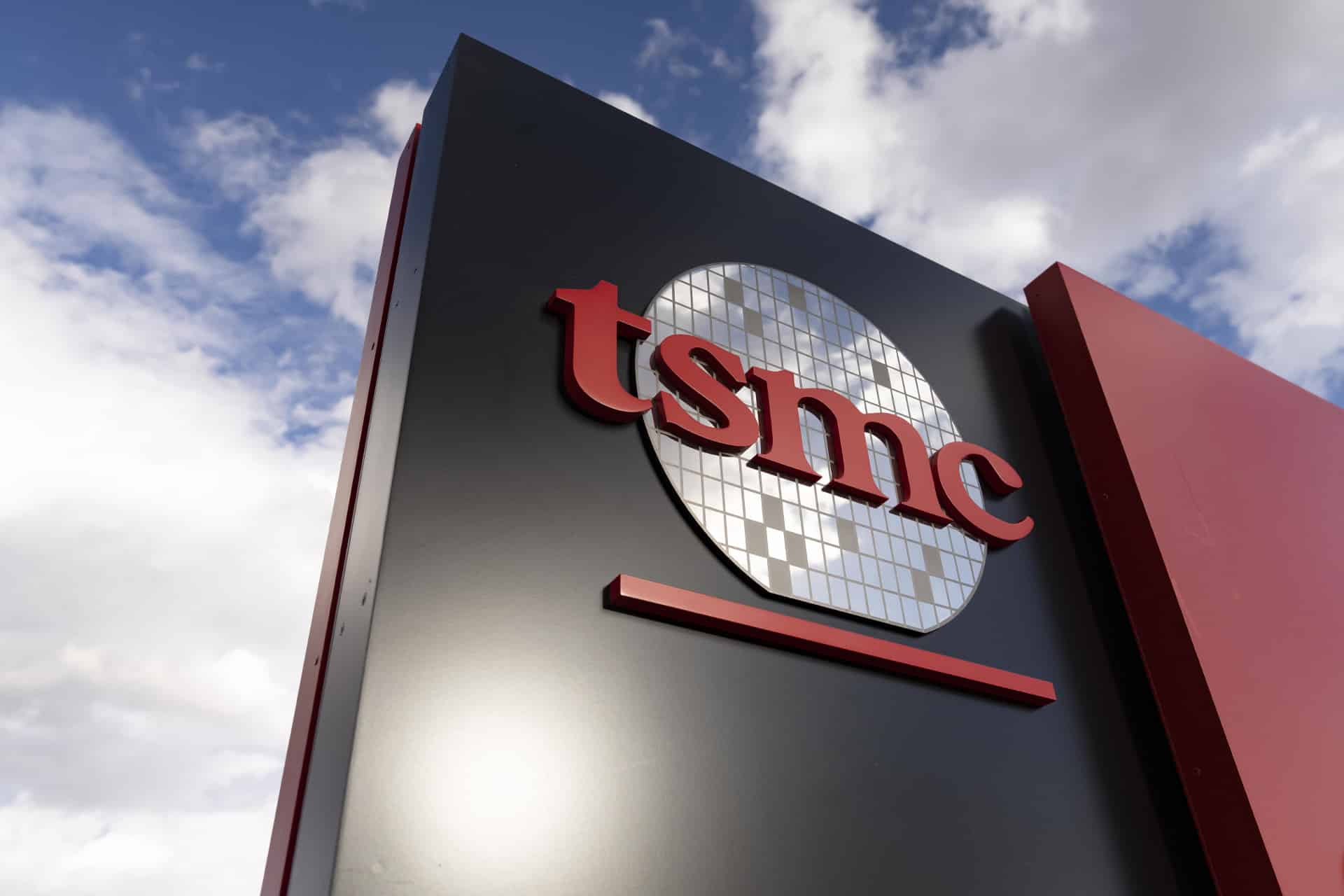 A sign featuring the TSMC logo, with red letters and a stylized silicon wafer graphic, stands against a partly cloudy sky—symbolizing the surge in TSMC AI chip demand.