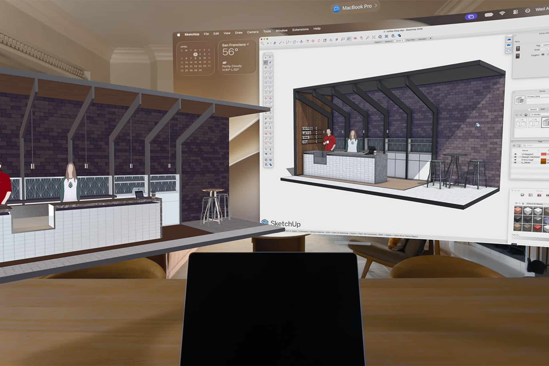 A laptop on a wooden desk displays a 3D café interior design in SketchUp, with the modeling interface on a large screen and a MacBook Pro in the background—perfect for exploring concepts before showcasing them on Apple Vision Pro.