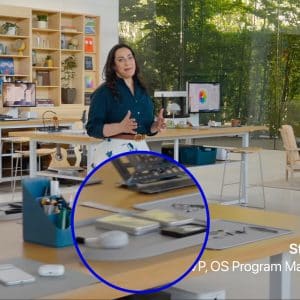A woman stands in a modern office with large windows and shelves behind her. In the foreground, a table displays tech devices, including an iPad Fold highlighted with a blue circle. Text reads "Stacey Ford, VP, OS Program Management.